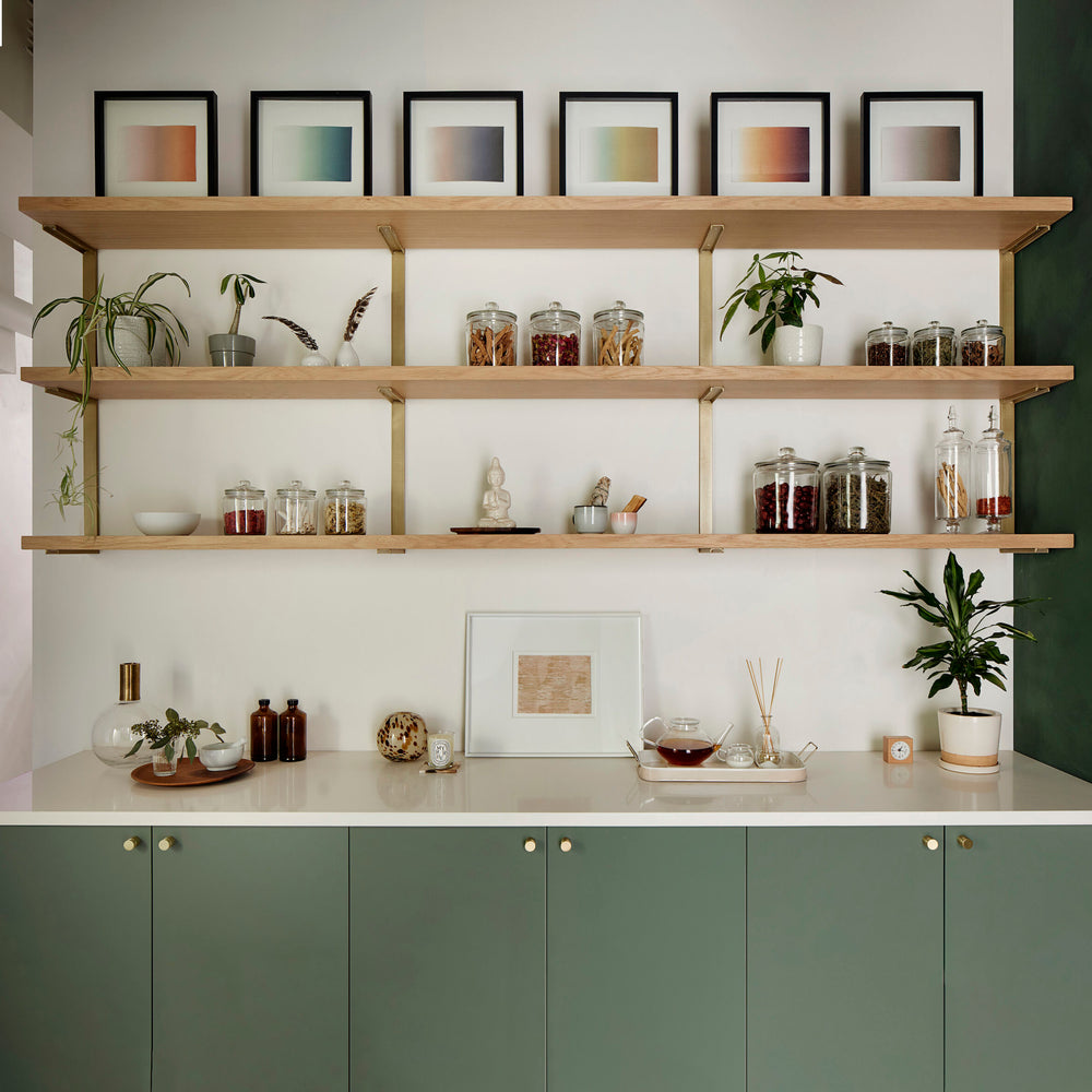 wall mounted shelving above green cabinetry. apothecary style shelves with brass wall mounted brackets and solid wood shelves by vault furniture