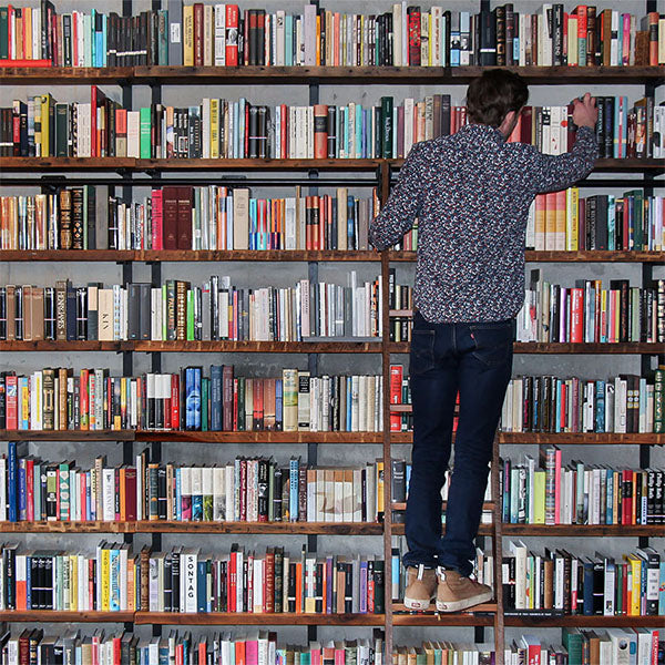 wall-mounted barnwood bookshelves full of books with rolling ladder. Man reaching for book on ladder.