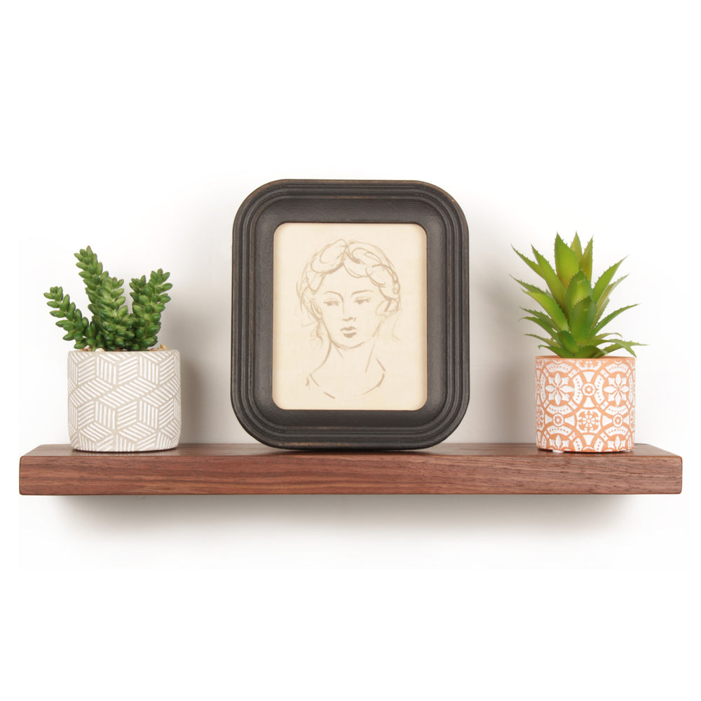 Black Walnut floating shelf ledge. Small picture ledge crafted from solid wood and steel. Small shelf to displaying framed drawing of woman's face and succulent plants. Small Wall mounted wood shelf handmade in USA from black walnut wood and American steel bracket. Vault Furniture