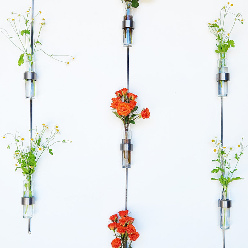 flowers in vertical wall-mounted glass vase with steel holder on white background