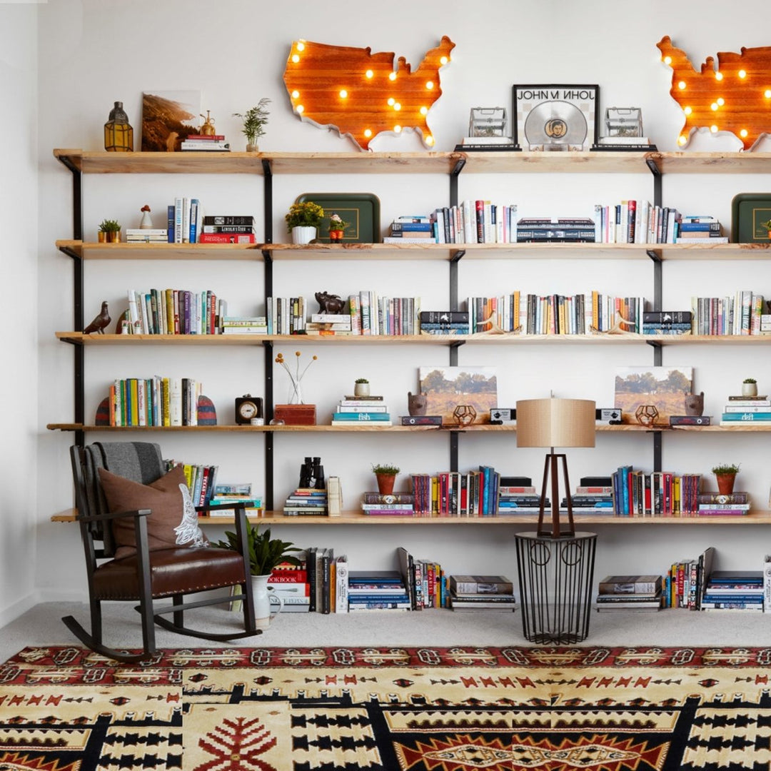Modern wall-mounted bookshelves with solid wood shelves and black steel brackets, styled with books, plants, décor, and accent lighting in a living room