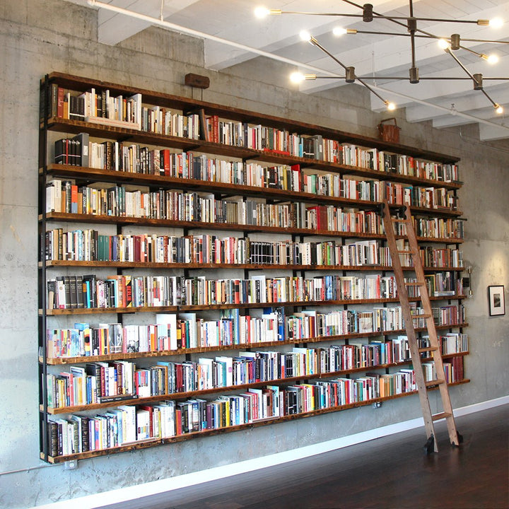 Large bookshelf filled with books against a concrete wall with a rolling ladder 