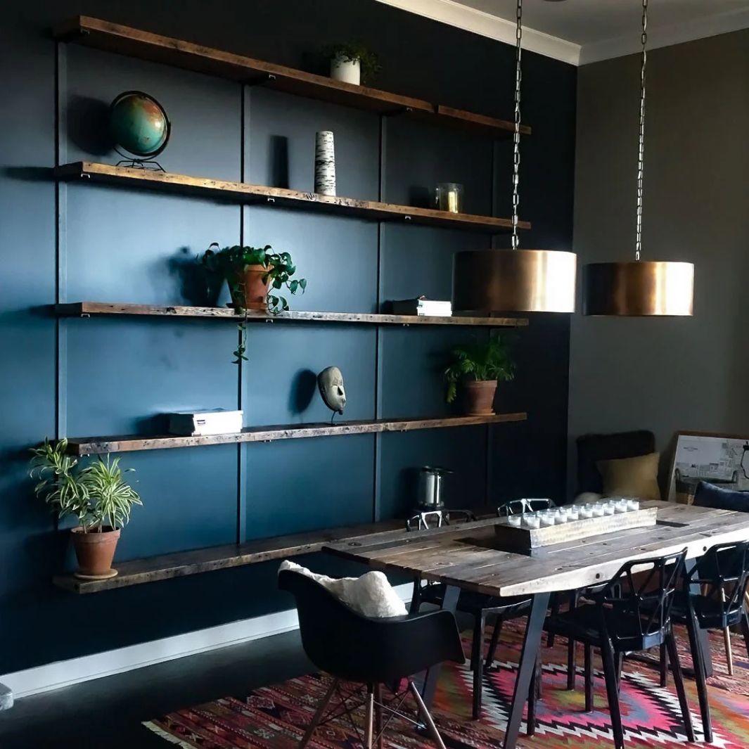 Moody modern living room and dining room with solid wall-mounted reclaimed pine wood shelves and steel brackets, a large heavy-duty floating bookshelf. 