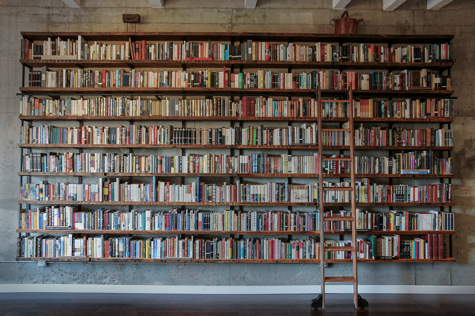 wall-mounted Bookshelf filled with books and a ladder in a room with wooden beams.
